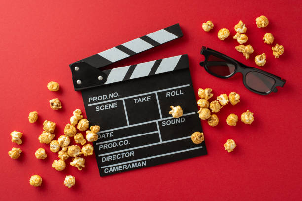 istock Love is in the Reel: Top view of a clapperboard, 3D glasses, scattered popcorn on a vibrant red surface, teasing a romantic film debut 1832851705