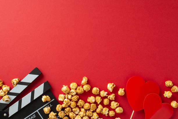 istock Romantic Movie Night: Overhead shot of a clapperboard, popcorn, and heart-shaped decor on a red backdrop, setting the scene for a love-filled film premiere 1832852111