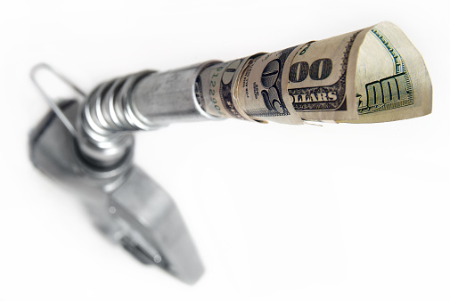 Image of money coming out of gas nozzle. The image is illustrating the high price of gasoline. Very shallow depth of field, money is in focus and quickly fades.