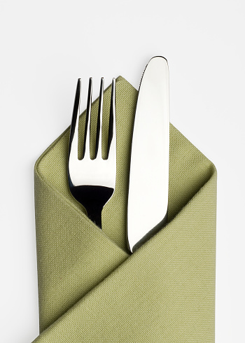 A studio shot of a knife and fork placed in a green serviette on a white background with Clipping Path and shadows
