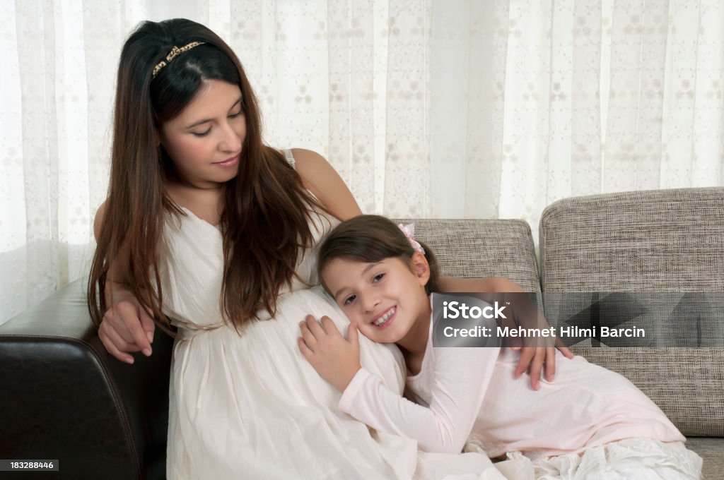 Donna incinta con la figlia sul divano - Foto stock royalty-free di Bambino piccolo