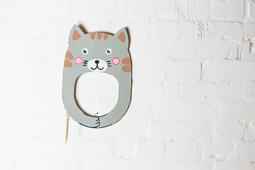 Bright cardboard mask on a white brick wall. Consept card. Cat