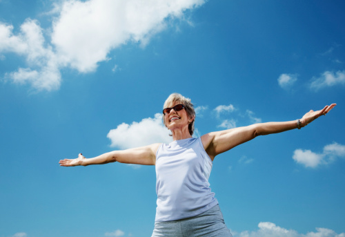 Portrait of an smiling mature lady with her hand stretched out against the sky - Outdoor