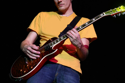 Rock n'Roll guitarist jams on his instrument on stage during a live show (natural black isolated background).