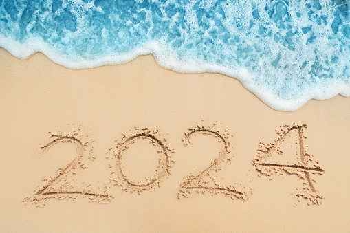 Happy New Year 2024 text on tropical beach sand and turquoise water of caribbean sea.