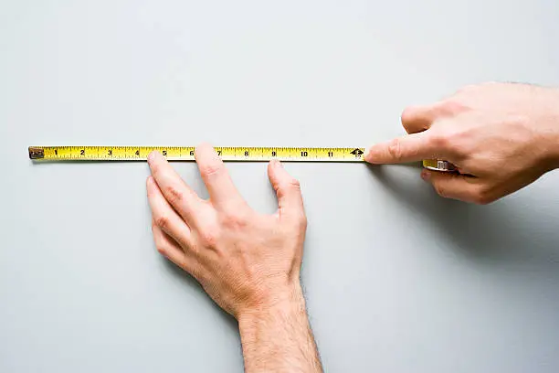 Man stands holding measuring tape against the wall