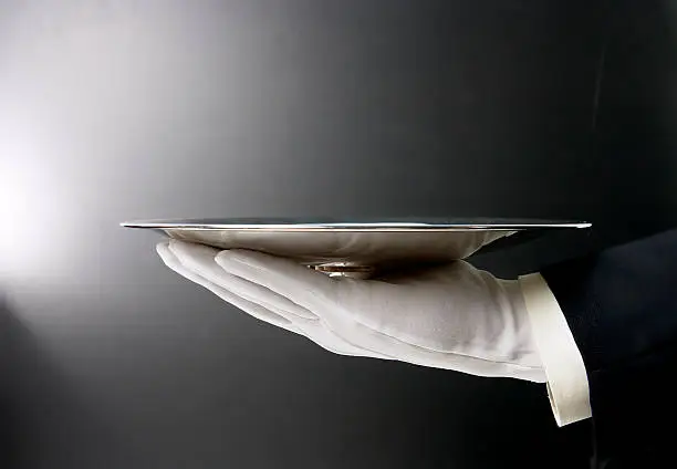 Butler's gloved hand presenting empty sivler tray on black background