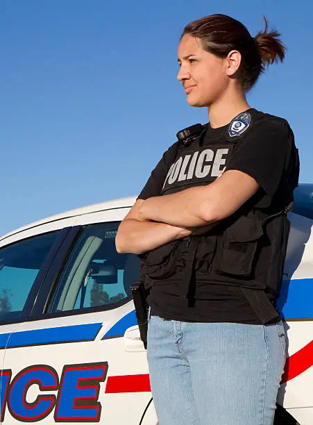 A Hispanic police woman standing against her car