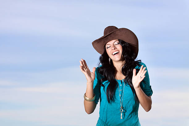 Cowgirl laughing or singing with eyes closed. Sky background.