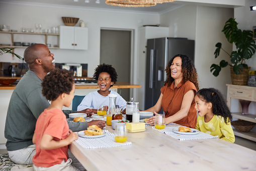 Parents and their adorable young children laughing while having breakfast together at their kitchen table in the morning