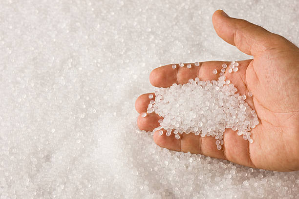 A hand sifting through a pile of clear plastic resin pellets stock photo