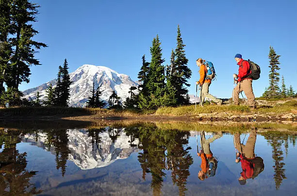 "Two hikers walk by a small pond with Mt. Rainier behind. Mt. Rainier National Park, Washington State."