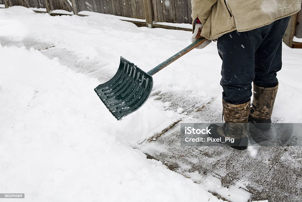 A man in boots shoveling snow from a sidewalk Man shovels snow from sidewalk in the year of La Nina (there's bound to be more snow in the forecast!) (Standing Feet Closeup) Activity Stock Photo
