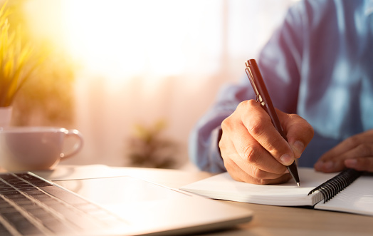 Close-up of man hand using writing pen memo on notebook paper or letter, diary on table desk office. Workplace for student, writer with copy space. business working and learning education concept.