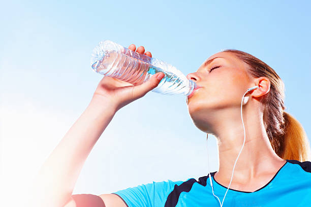 istock Young female athlete drinking water after jogging against sky 183297627