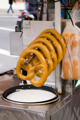 Rack of pretzels hanging over a pan of salt for sale on a street vendor's cart.