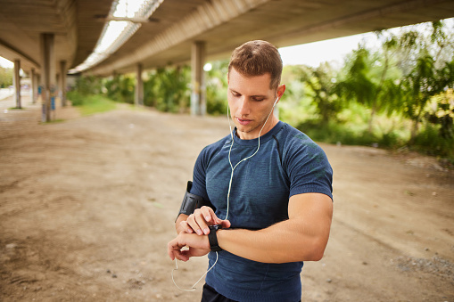 Male athlete looking at his smart watch or tracker under the bridge