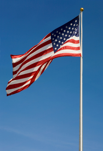 American flag waving on flagpole against blue sky in warm afternoon light