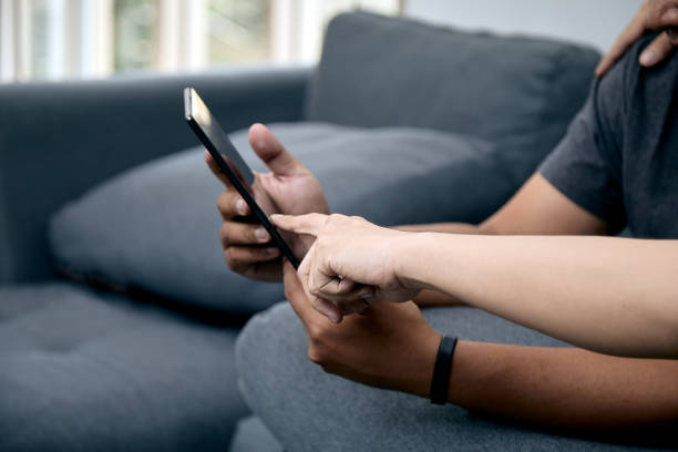 istock Two gay men holding and pointing digital tablet sitting on gray sofa 1833012120