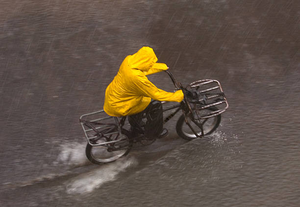 Cylcing in the rain Man in bright yellow raincoat cylcing through a flooded street. With visible raindrops. heavy rainfall stock pictures, royalty-free photos & images