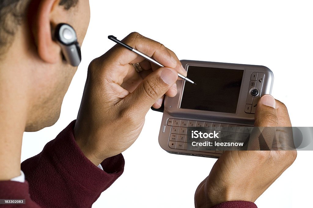 Man Using Stylus on PDA and Wireless Phone "Over the shoulder of a man with a wireless phone piece in his ear, using a handheld pda device with a stylus in hand.  Focus is on the handheld and hands. Head and earpiece are out of focus.   Isolated in white.Also see:" Bluetooth Stock Photo