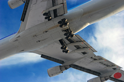 Closeup shot of a Boeing 747 airplane from below, blue cloudy sky in the back