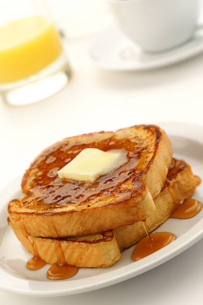 A close-up of French toast on a white plate High-resolution digital capture of a plate containing two slices of french toast with butter and syrup, a glass of orange juice, and a cup of coffee, all shot on a sunny white table.  french toast stock pictures, royalty-free photos & images