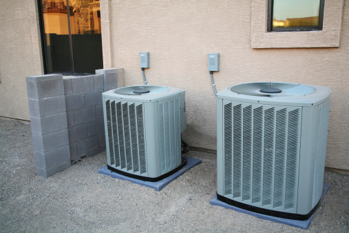 A couple of brand new air conditioners sitting next to a new home. The block wall to the left of them has not been finished yet. These are Crane Air Conditioners.