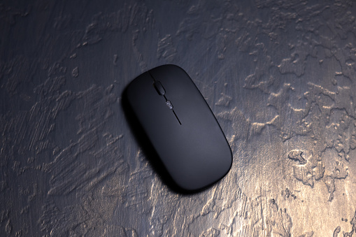 Black wireless minimalist mouse for laptop on the black background. Modern technology device.