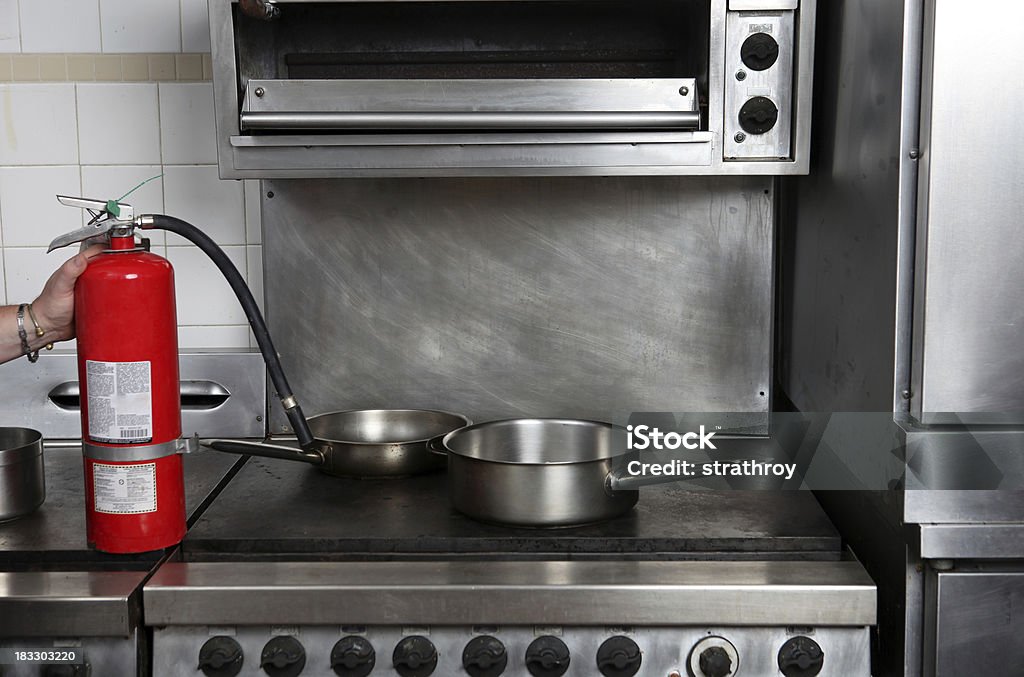 Man's Hand Holding a Fire Extinguisher Professional kitchen and a fire extinguisher. Restaurant fire safety concept. Commercial Kitchen Stock Photo