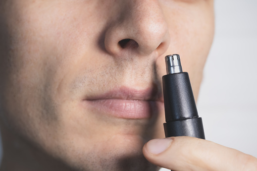 Personal Care Concept. Man tending to his nasal hair with an electric trimmer. Close up view.