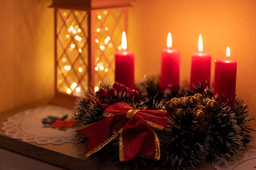 Candles lit on Christmas advent wreath with red berries and evergreen boughs, all four candles lit