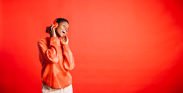 Happy young woman dancing and singing while wearing wireless headphones in a studio. Woman listening her favourite music playlists.