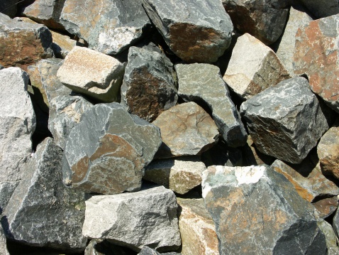 A colorful mixture of large rocks used as shoreline riprap next to a bridge.  Taken looking straight down.