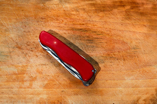 Red pocket knife and multi-tool on wood board