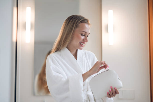 istock Smiling young woman in white robe holding a bag cosmetics 1833089528