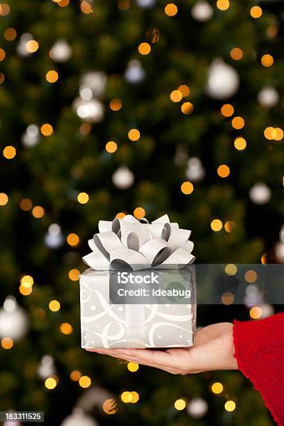 Young Woman Holding Christmas Gift With Lights And Tree Stock Photo - Download Image Now