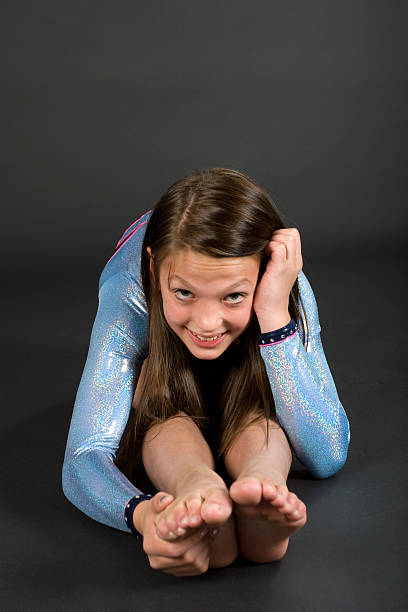 Young female teen gymnast sitting and leaning forward over legs looking at camera.