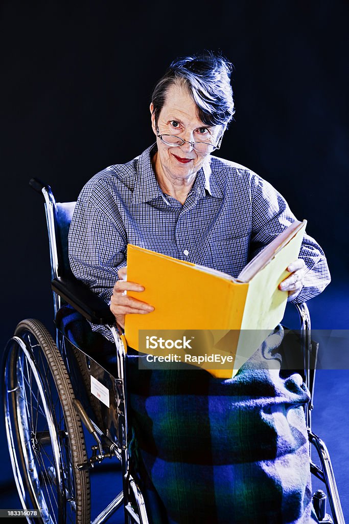 Velha mulher em cadeira de rodas looks up sorridente do livro amarelo - Royalty-free 60-69 Anos Foto de stock