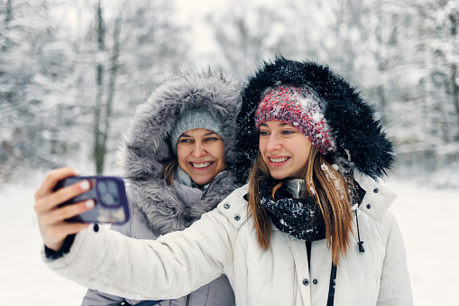 Teenage girls and her mother are enjoying snow on winter day. They are walking in the forest and taking selfies.\nShot with Canon R5