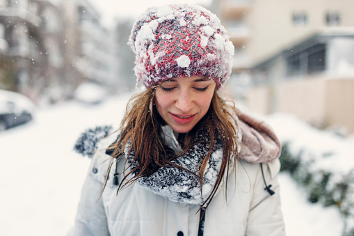 Portrait of a beautiful young woman wearing scarf and a a hat on a cold winter day during snow