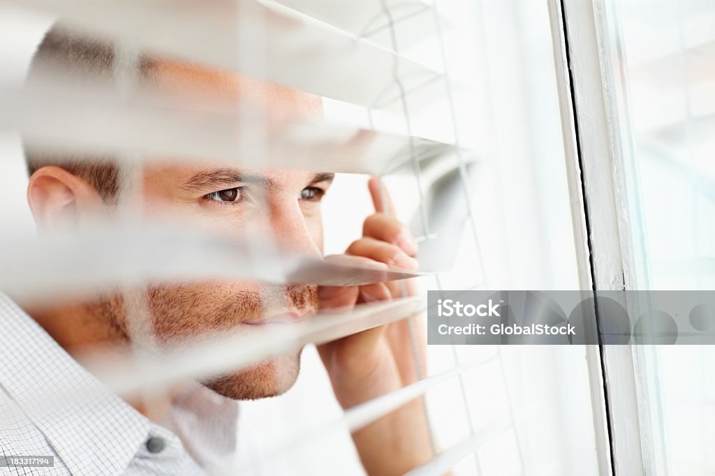 Young man peeking out of the window blinds Closeup portrait of a young man peeking out of the window blinds 20-29 Years Stock Photo