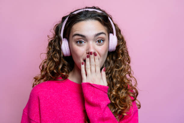 surprised young woman in pink sweater listening to music with headphones on pink background - news of the world imagens e fotografias de stock