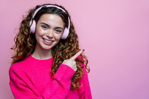 Portrait of a beautiful young woman listening to music with headphones on a pink background