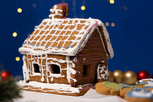 Christmas house made of gingerbread cookies decorated with sugar icing on blue background with bokeh garland.