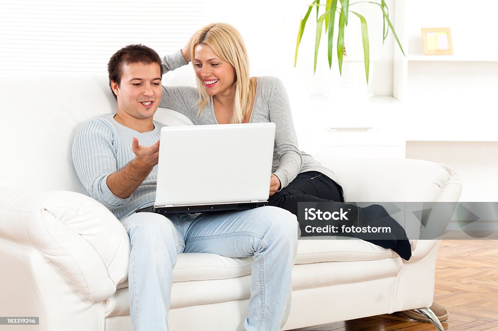 Couple à l'aide d'ordinateur portable assis sur le canapé à la Maison Blanche - Photo de Adolescent libre de droits