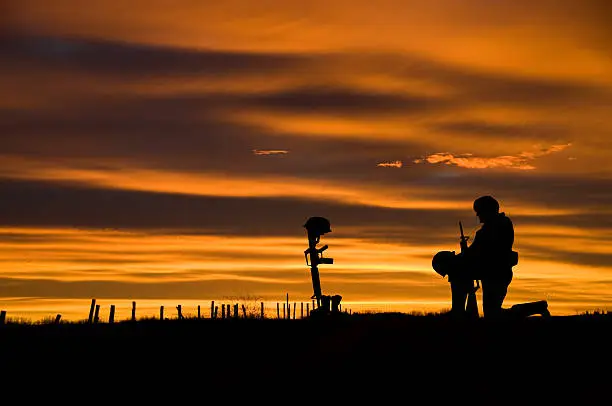 The battlefield grave of a fallen soldier with another soldier kneeling before it. Copy space