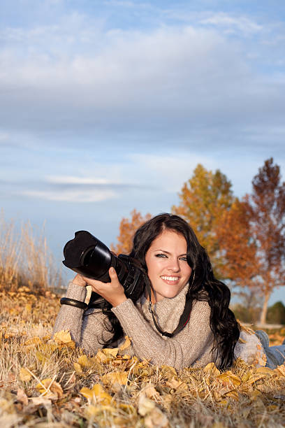 Happy Female Photographer Lying on Ground Outdoors Holding Camera