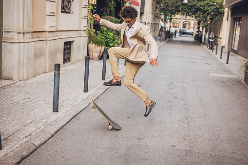 Elegant man in a suit doing a trick with skateboard in city.