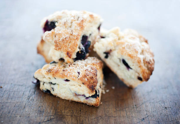 Four Blueberry scone pastries on a wooden table A fresh batch of blueberry scones shot with shallow focus on a rustic cutting board. scone photos stock pictures, royalty-free photos & images